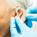 Close-up of a hearing aid being fitted on an older person's ear.
